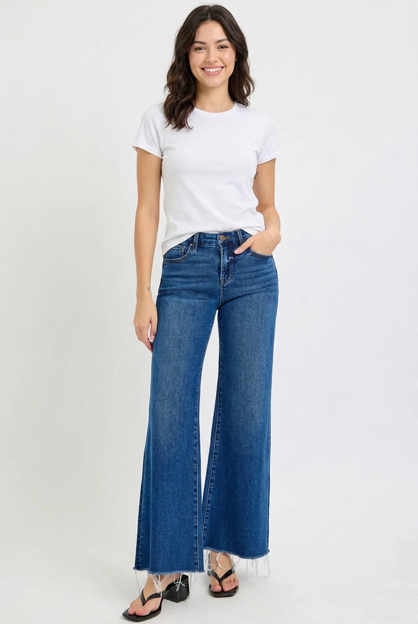 Smiling young adult model wearing Heather dark wide-leg jeans with frayed hems, a white tee and black sandals.